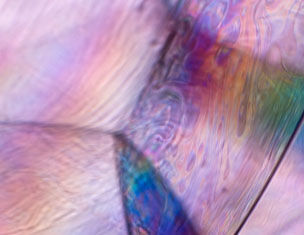Close-up of a colorful, iridescent surface with swirling patterns and smooth textures, reflecting light in pastel hues.