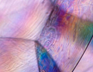 Close-up of a colorful, iridescent surface with swirling patterns and smooth textures, reflecting light in pastel hues.