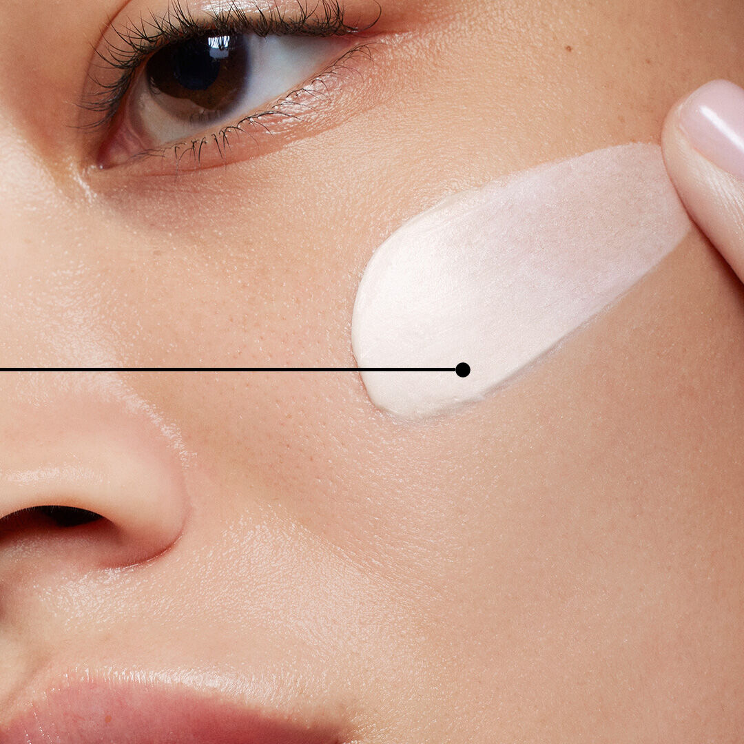 Een close-up van een gezicht waarop een romige huidverzorgingsproduct wordt aangebracht.