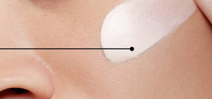 Een close-up van een gezicht waarop een romige huidverzorgingsproduct wordt aangebracht.