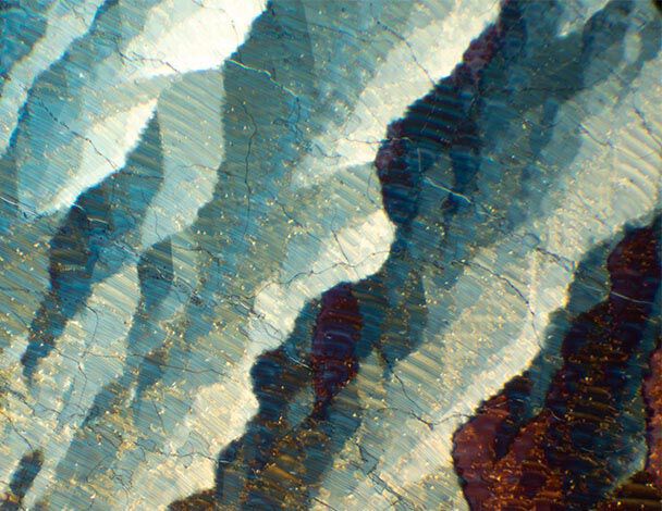 Details colores et textures d'un cristal, presentant des stries bleues, blanches et ocres sous une lumiere brillante.