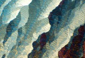 Details colores et textures d'un cristal, presentant des stries bleues, blanches et ocres sous une lumiere brillante.