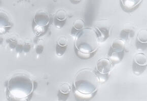 Des gouttes d'eau transparentes flottent sur un fond clair, creant un effet de texture et de lumiere.