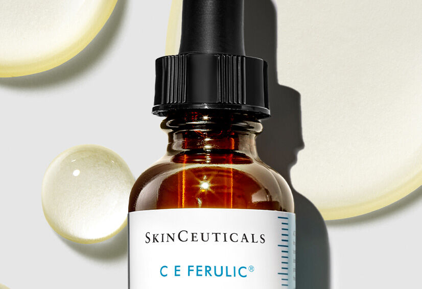 Flesje SkinCeuticals C E Ferulic serum op een lichte achtergrond met druppels en olievlekken.
