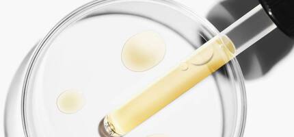 Een pipet met een gele vloeistof boven een petrischaal met druppels van dezelfde vloeistof.