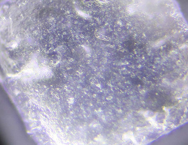 Close-up view of a translucent crystal, showcasing its surface texture and reflective properties under light.