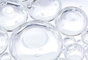 Gros plan sur des bulles d'air transparentes a la surface d'un liquide clair, creant un effet de legerete et de fraicheur.