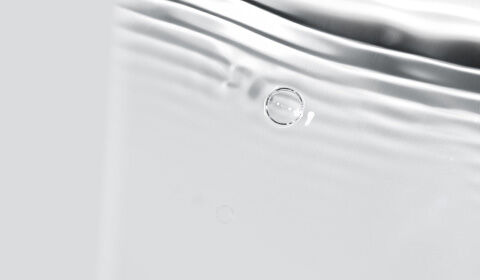 Abstract close-up of soft, flowing water with gentle ripples and bubbles on a light background.