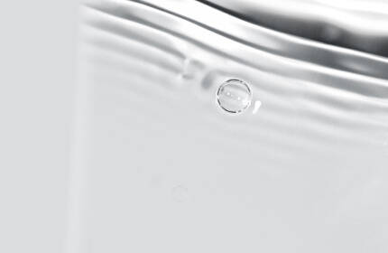 Abstract close-up of soft, flowing water with gentle ripples and bubbles on a light background.