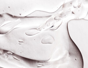 Close-up of a translucent gel with droplets, creating a smooth, flowing texture on a light background.