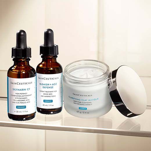 Three SkinCeuticals skincare products are displayed: two amber dropper bottles labeled "Silymarin CF" and "Blemish + Age Defense," and a jar labeled "Clarifying Clay Masque." The products feature a clean, modern design with white and teal labels.