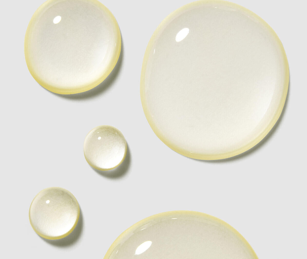 Drops of clear liquid in varying sizes, reflecting light against a soft gray background.