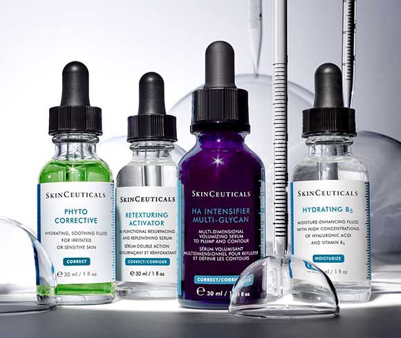 Vier flacons met huidverzorgingsserums van SkinCeuticals, waaronder Phyto Corrective, Retexturing Activator, HA Intensifier Multi-Glycan en Hydrating B's, met druppelaars en een glazen pipet op een lichte achtergrond.