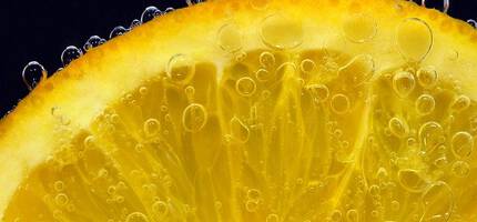 Close-up of a lemon slice with bubbles forming around its surface, showcasing vibrant yellow hues and juicy texture against a dark background.