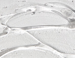 Close-up of clear gel or liquid on a textured white surface, displaying smooth contours and reflections.
