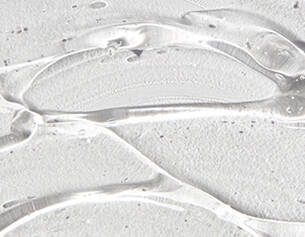 Close-up of clear gel or liquid on a textured white surface, displaying smooth contours and reflections.