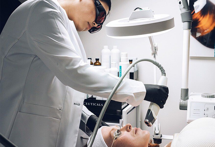 Een huidtherapeut voert een behandeling uit op een patient in een schoonheidssalon, terwijl de patient op een behandeltafel ligt.