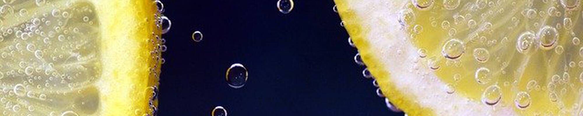 Tranches de citron avec des bulles d’air sur un fond sombre, creant un effet rafraichissant et petillant.