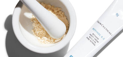 A white mortar and pestle containing a fine powder, next to a tube of SkinCeuticals Retinol 0.5 skincare cream.