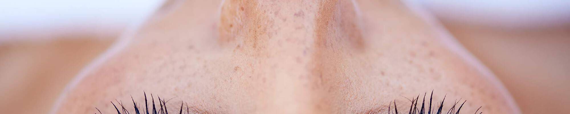 Gros plan du visage avec taches de rousseur et longs cils, concentre sur le nez et les yeux.