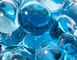 A close-up of shiny, translucent blue marbles layered on top of each other, creating a vibrant, reflective surface.
