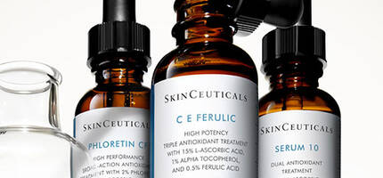 Drie flessen met huidverzorgingsserums van SkinCeuticals, waaronder C E Ferulic, Phloretin CF en Serum 10, staan op een schap met een pipet en een glazen houder.