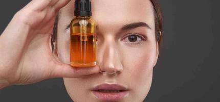 Een vrouw houdt een flesje gezichtsolie voor haar gezicht.